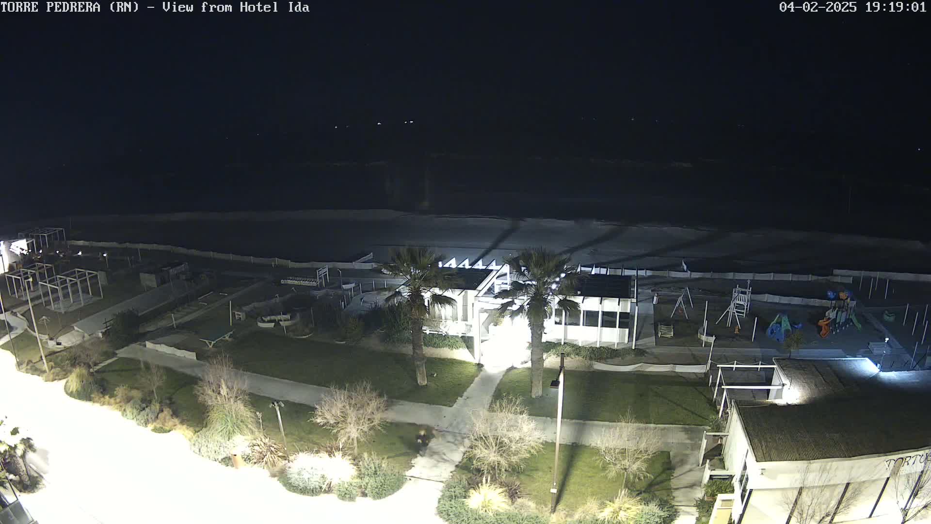 A nighttime, overhead view shows a beach, a playground, a beachfront building, and landscaping, all lit by artificial lights.
