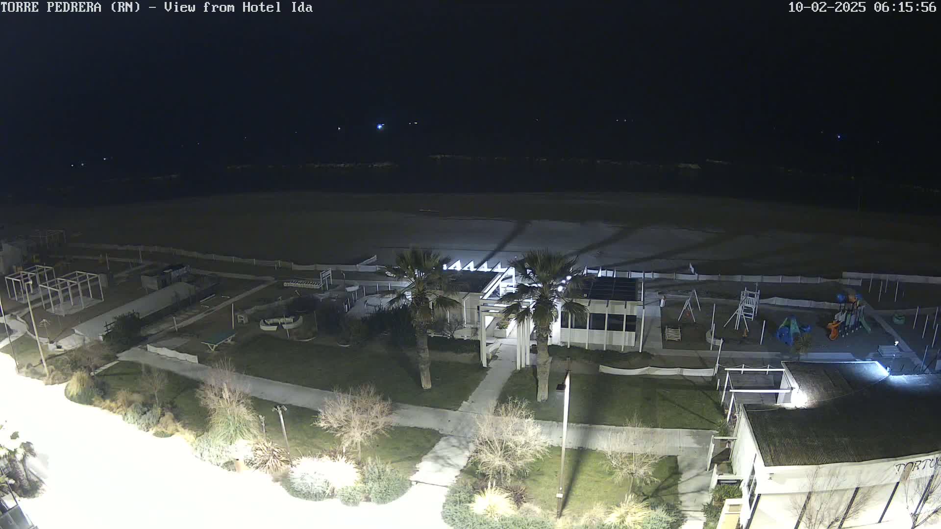 A nighttime, overhead view of a beach, playground, and beachfront building, with palm trees and sparsely vegetated areas visible.