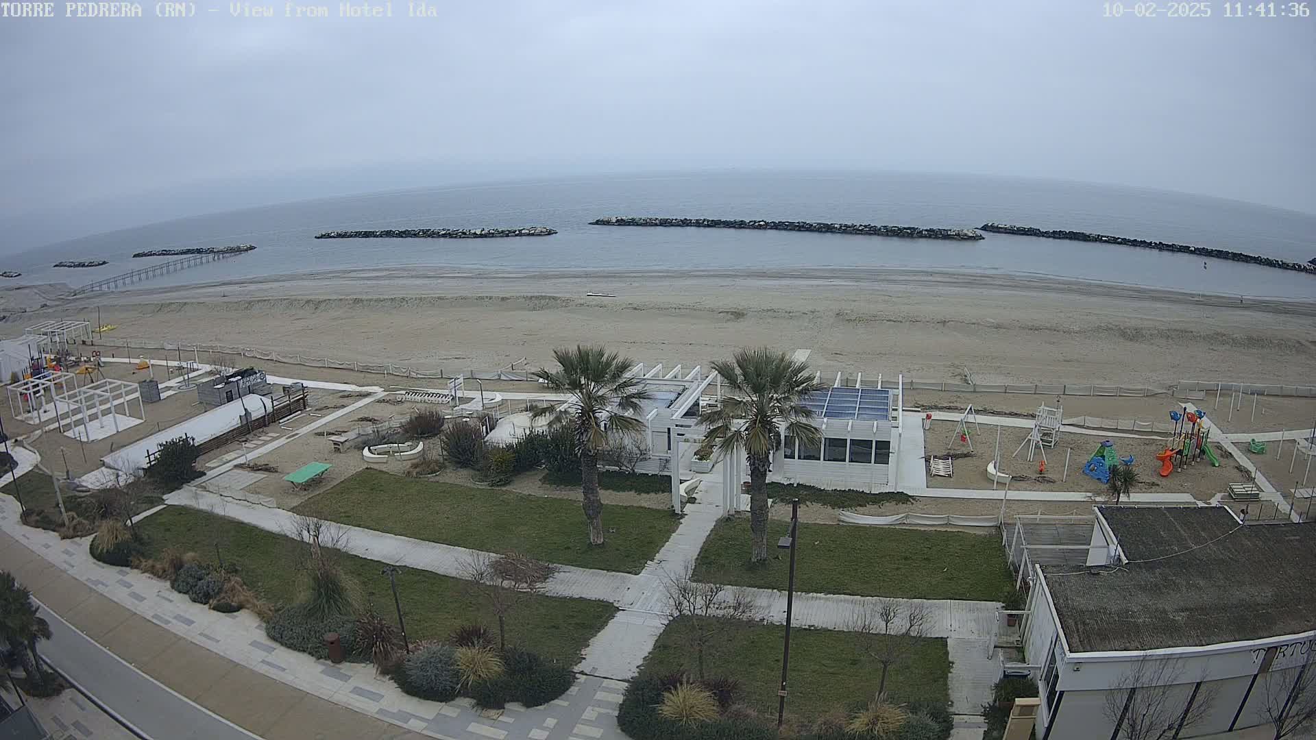 A beach with a playground and a white building is seen from above on an overcast day.