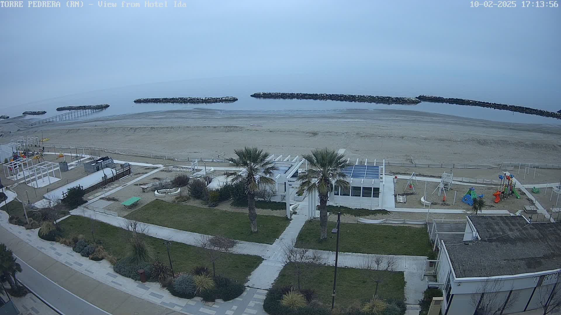 A beach with a playground and a white building is visible, with calm, overcast waters in the background.