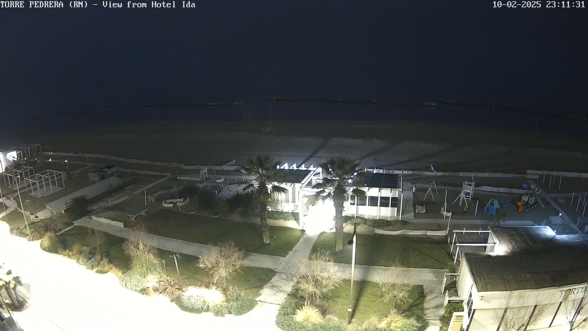 A nighttime, overhead view of a beach, playground, and buildings with palm trees, under a dark sky.