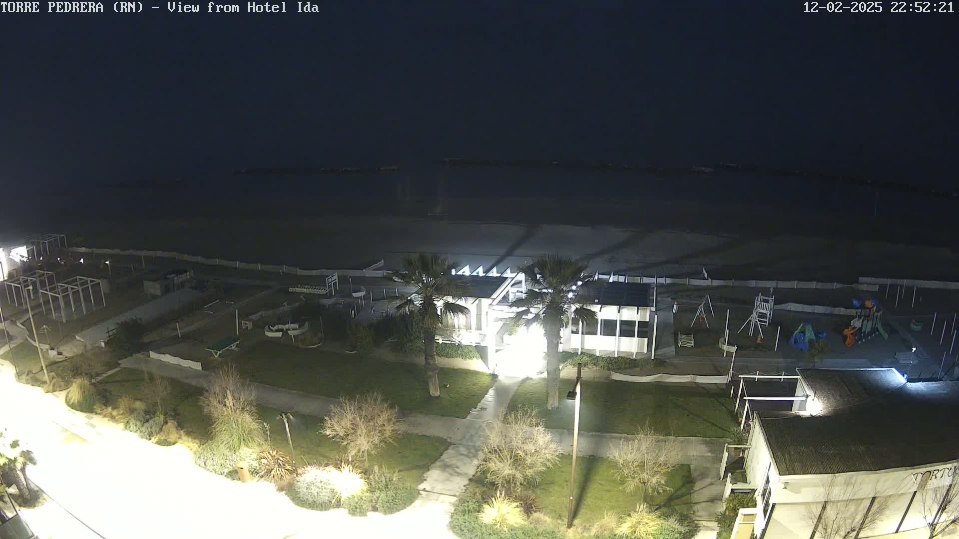 A nighttime aerial view of a beach area showing a building, playground, and palm trees under a dark sky.