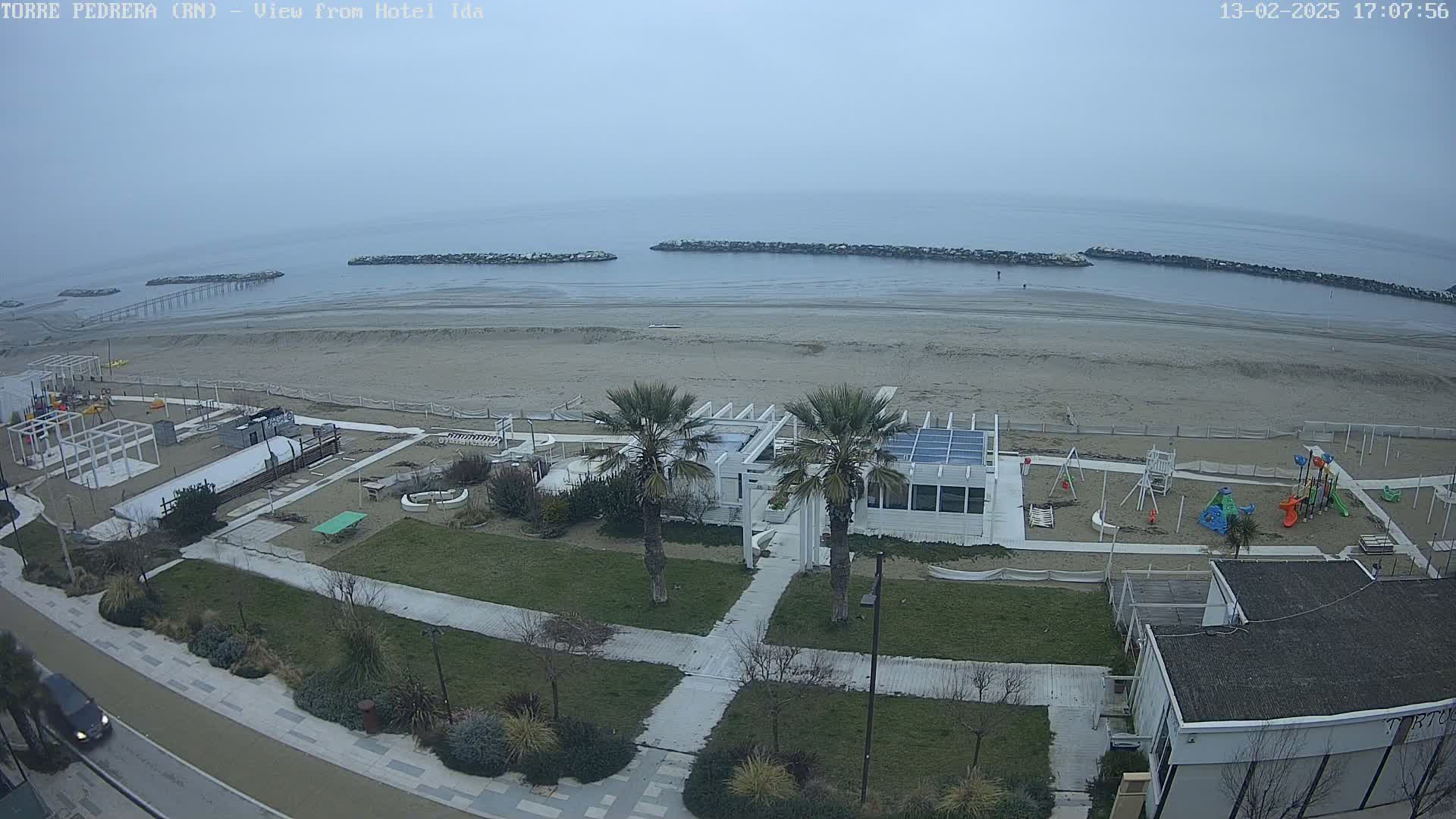 A beach with a playground and beachfront building is visible under an overcast sky.