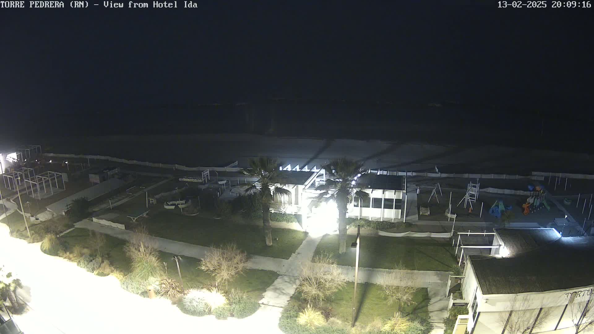 A nighttime view of a beach area with a building, playground, and some landscaping, under a dark sky.
