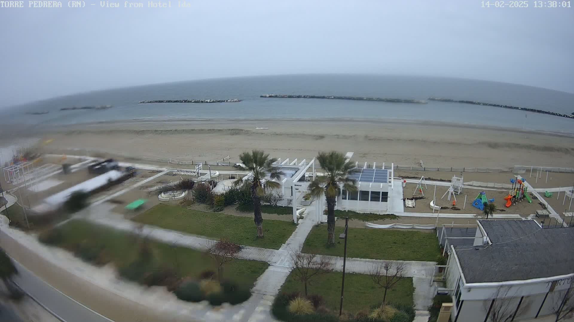 An overcast day at a beachside playground and restaurant area, with a calm sea visible in the background.