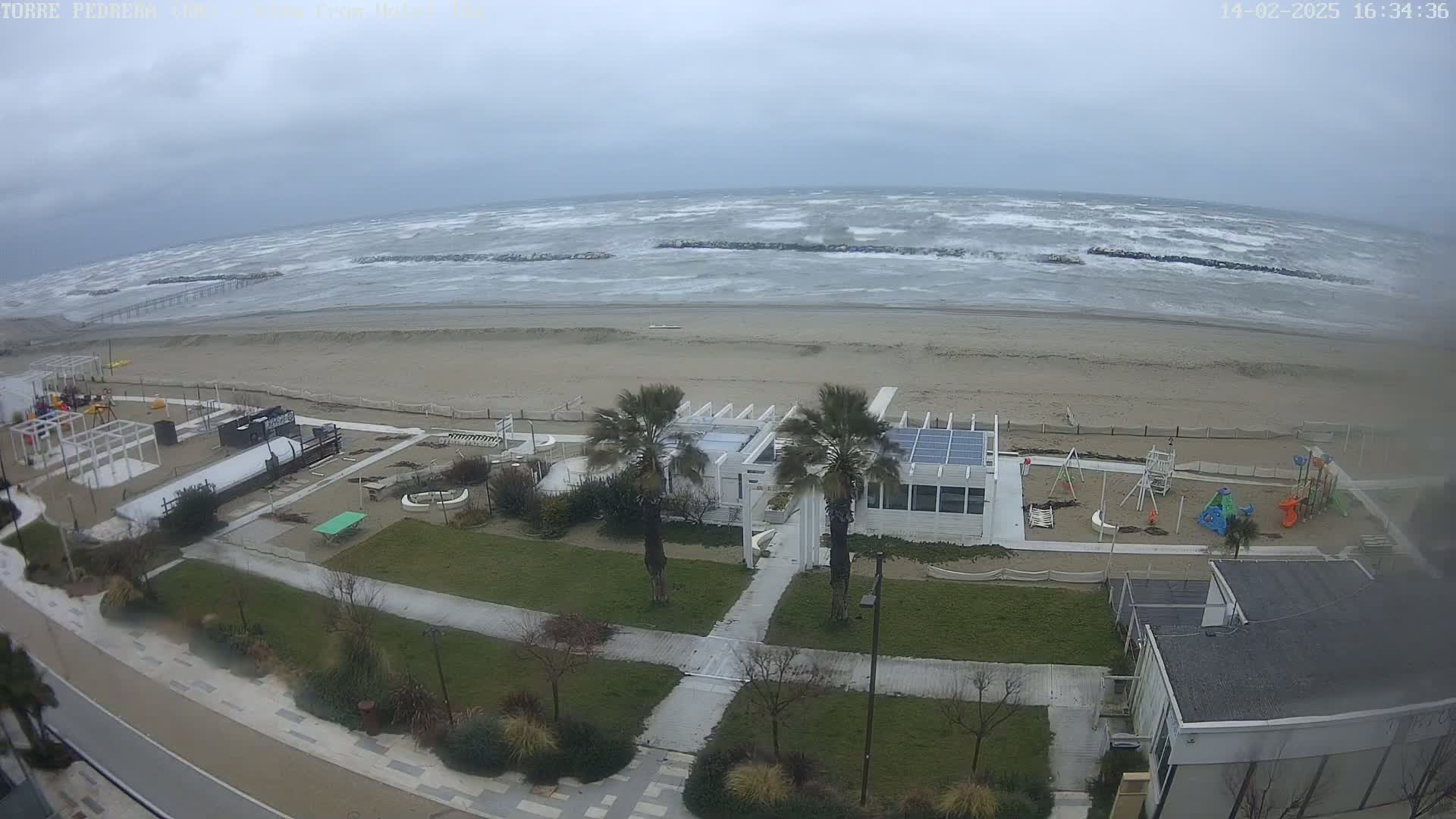 A beach with a playground and beachfront buildings is shown under an overcast sky with a choppy sea.
