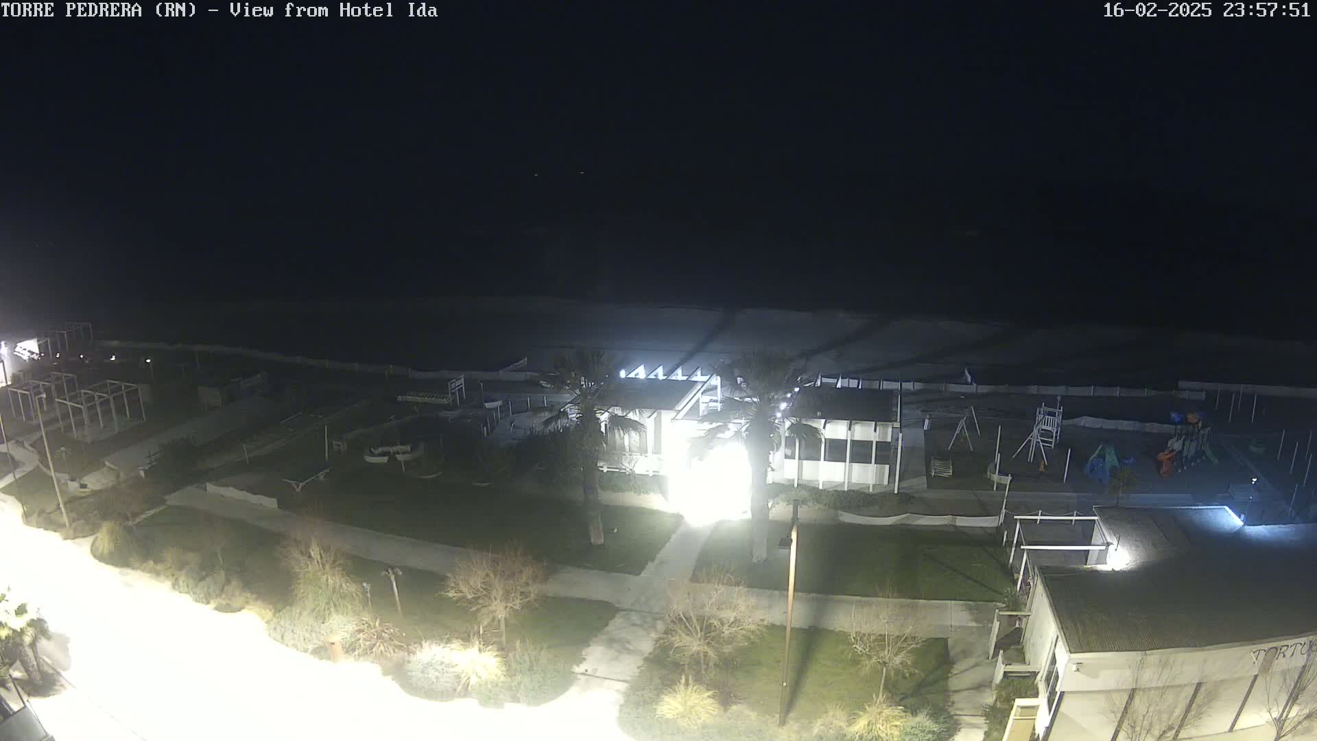A nighttime, high-angle view shows a beach, playground, and building complex illuminated by artificial lights.