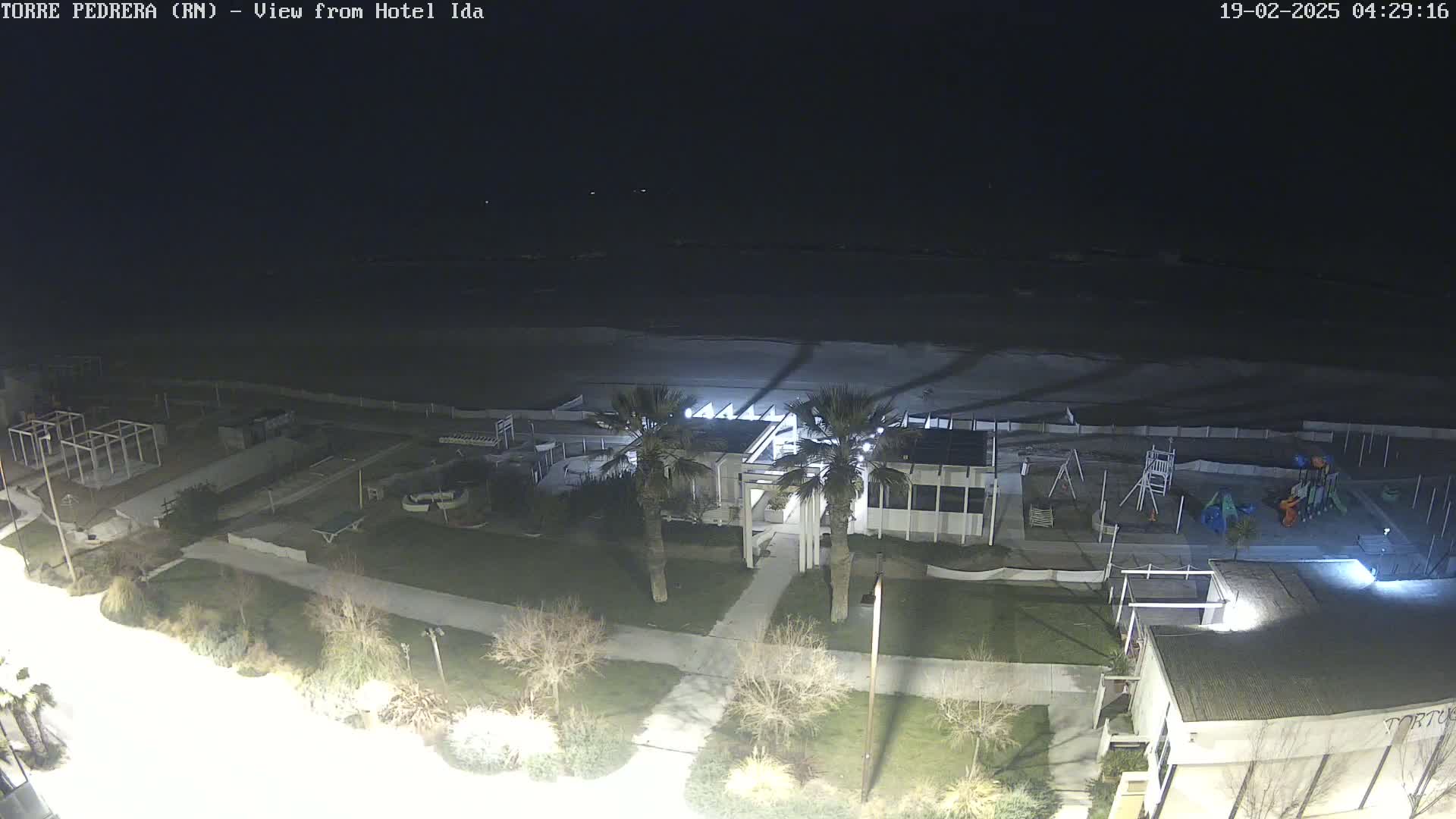 A nighttime view of a beach with a building, palm trees, and a playground, under a dark sky.
