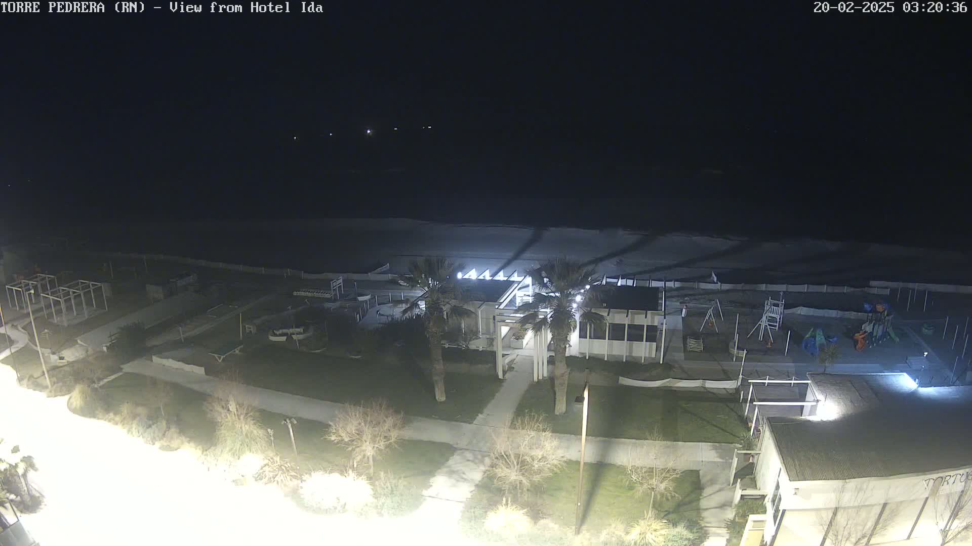 A nighttime, high-angle view of a beach area with a building, playground, and palm trees, under a dark sky.