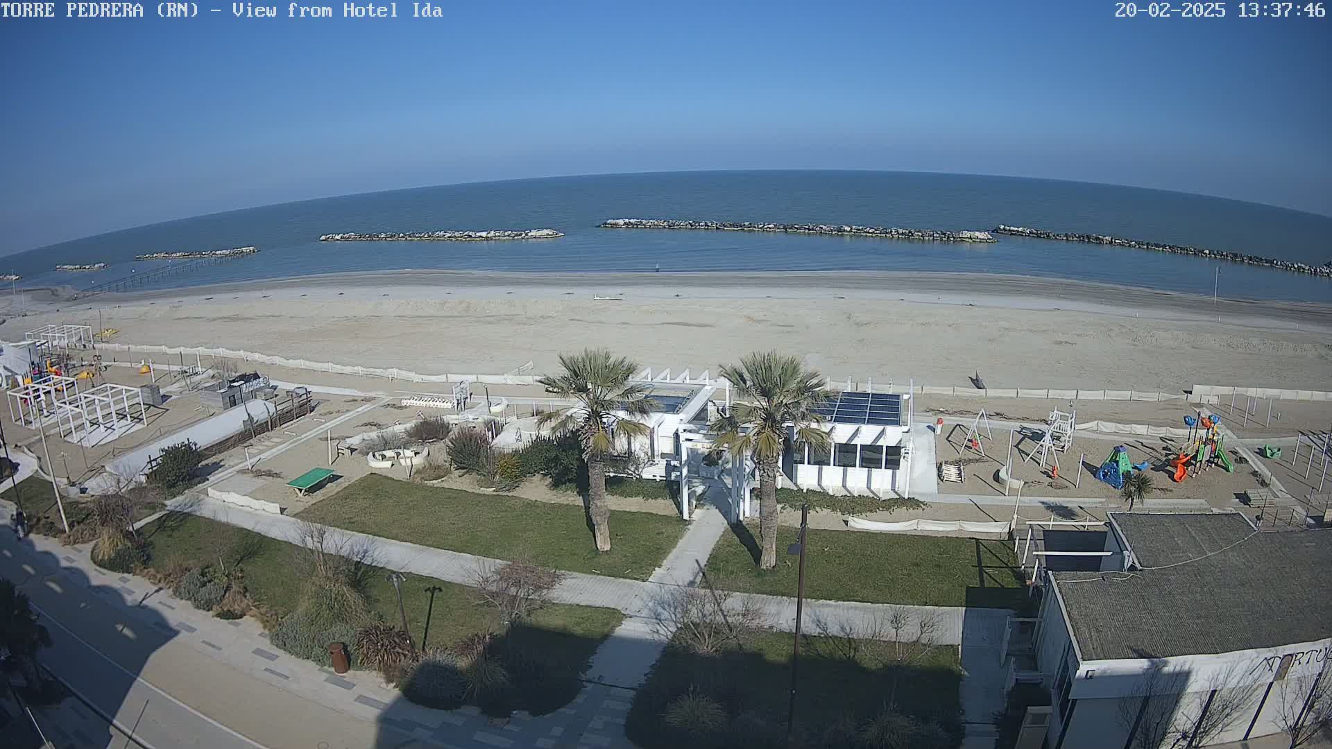 A beach with a playground and a building near palm trees is visible under sunny skies.
