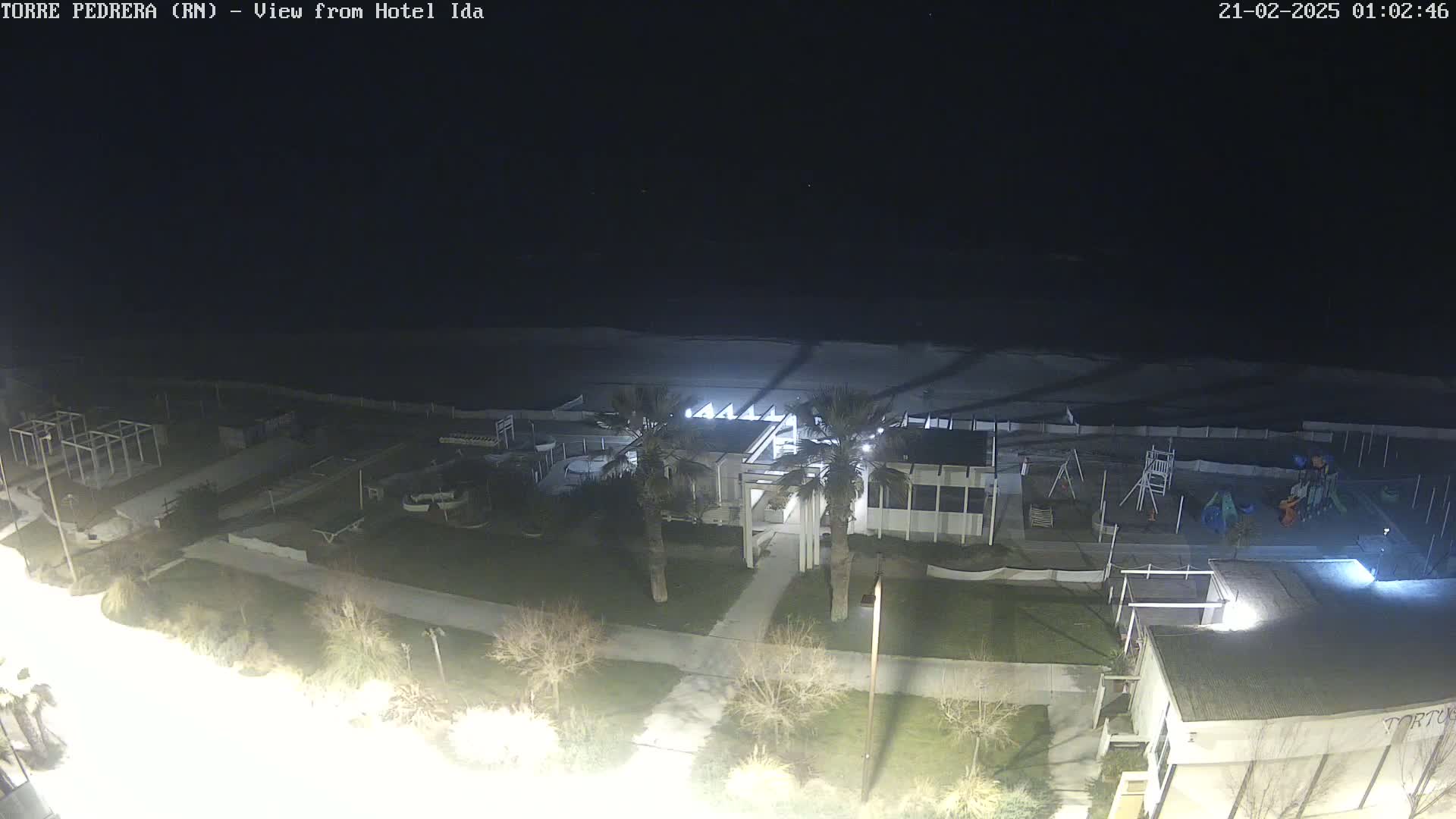 A nighttime aerial view of a beach with a building, playground, and palm trees, under a clear, dark sky.