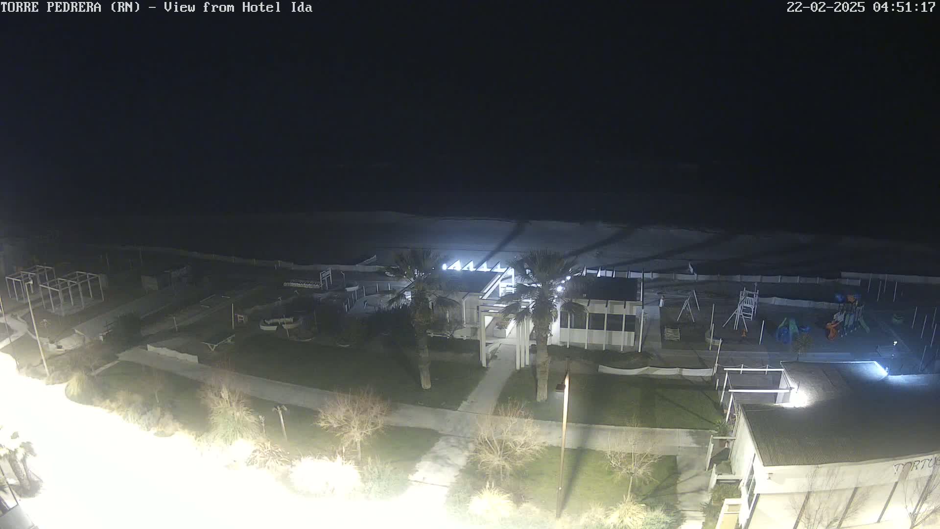 A nighttime view of a beach, playground, and building complex, illuminated by artificial lights, under a dark sky.
