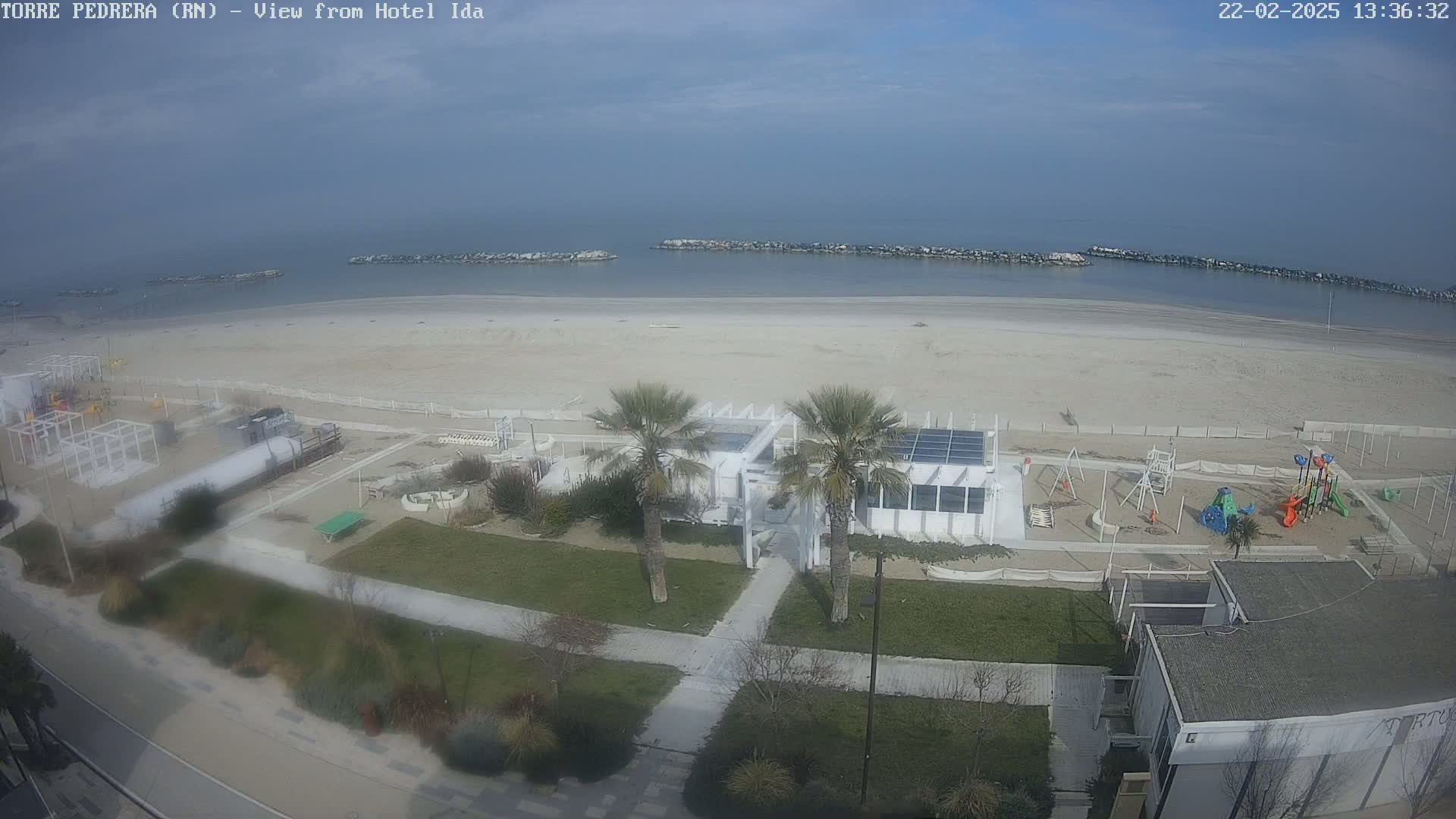 A beach with a playground and a white building is visible, under a mostly clear sky.