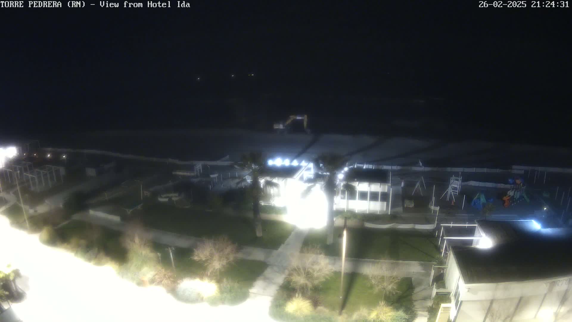 A nighttime, overhead view of a beach area with a playground and buildings, under dark skies.