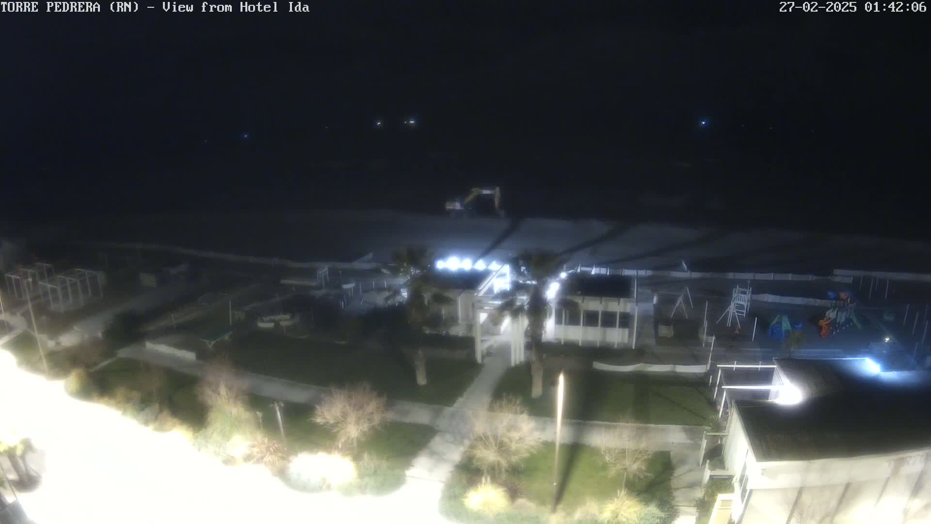 A nighttime, high-angle view shows a beach, playground, and buildings illuminated by artificial light.