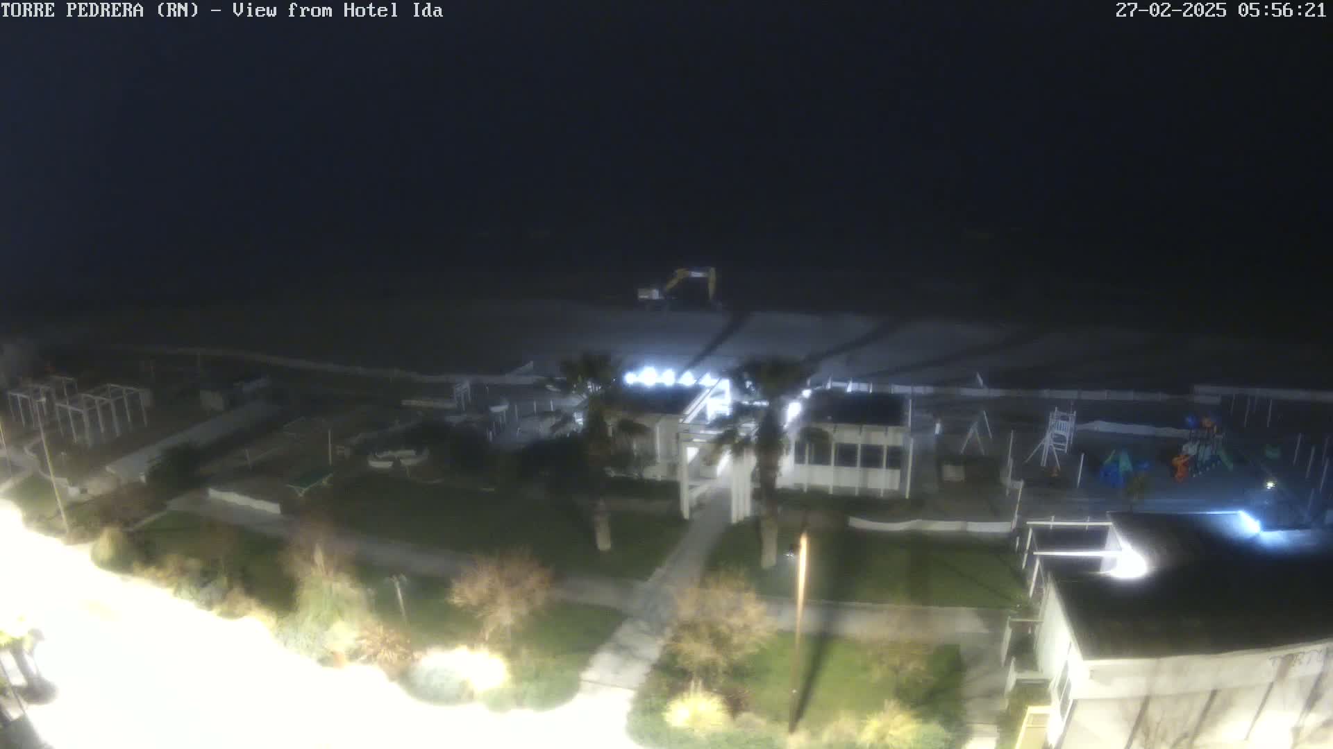 A nighttime, high-angle view of a beach area with buildings, landscaping, and playground equipment under a dark sky.