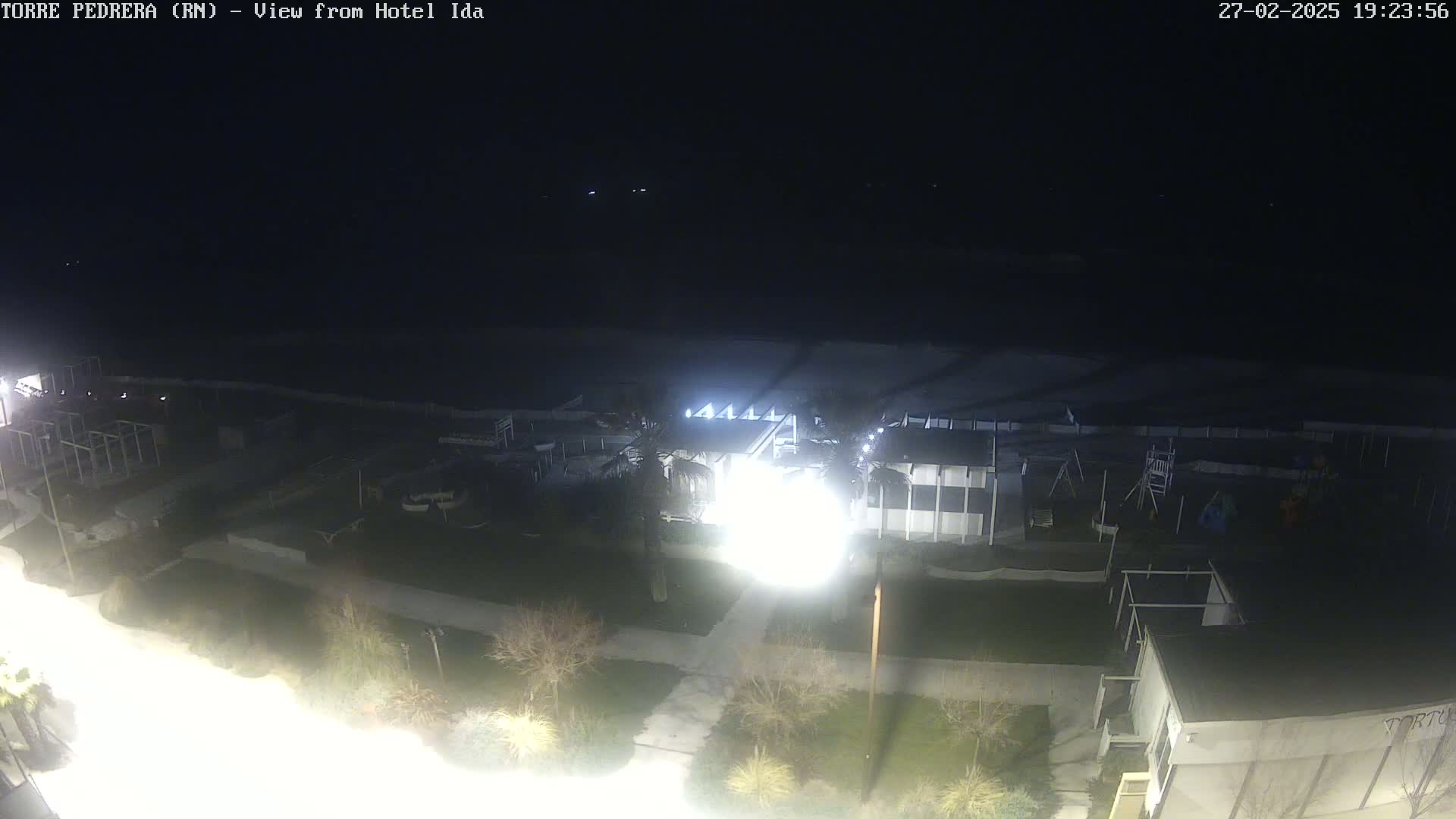 A nighttime, overhead view of a beach area with buildings, landscaping, and playground equipment under bright lights.