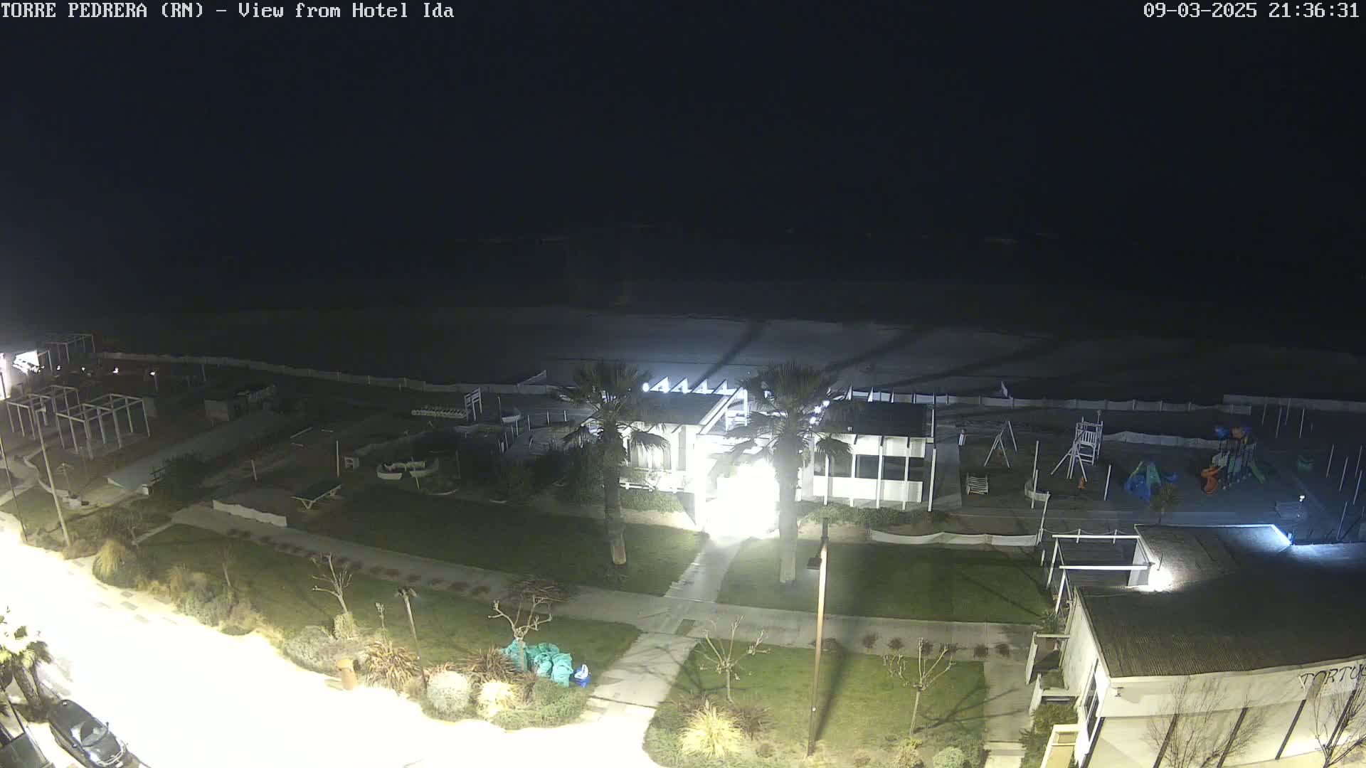 A nighttime view of a beach, playground, and beachfront building, lit by artificial lights under a clear, dark sky.