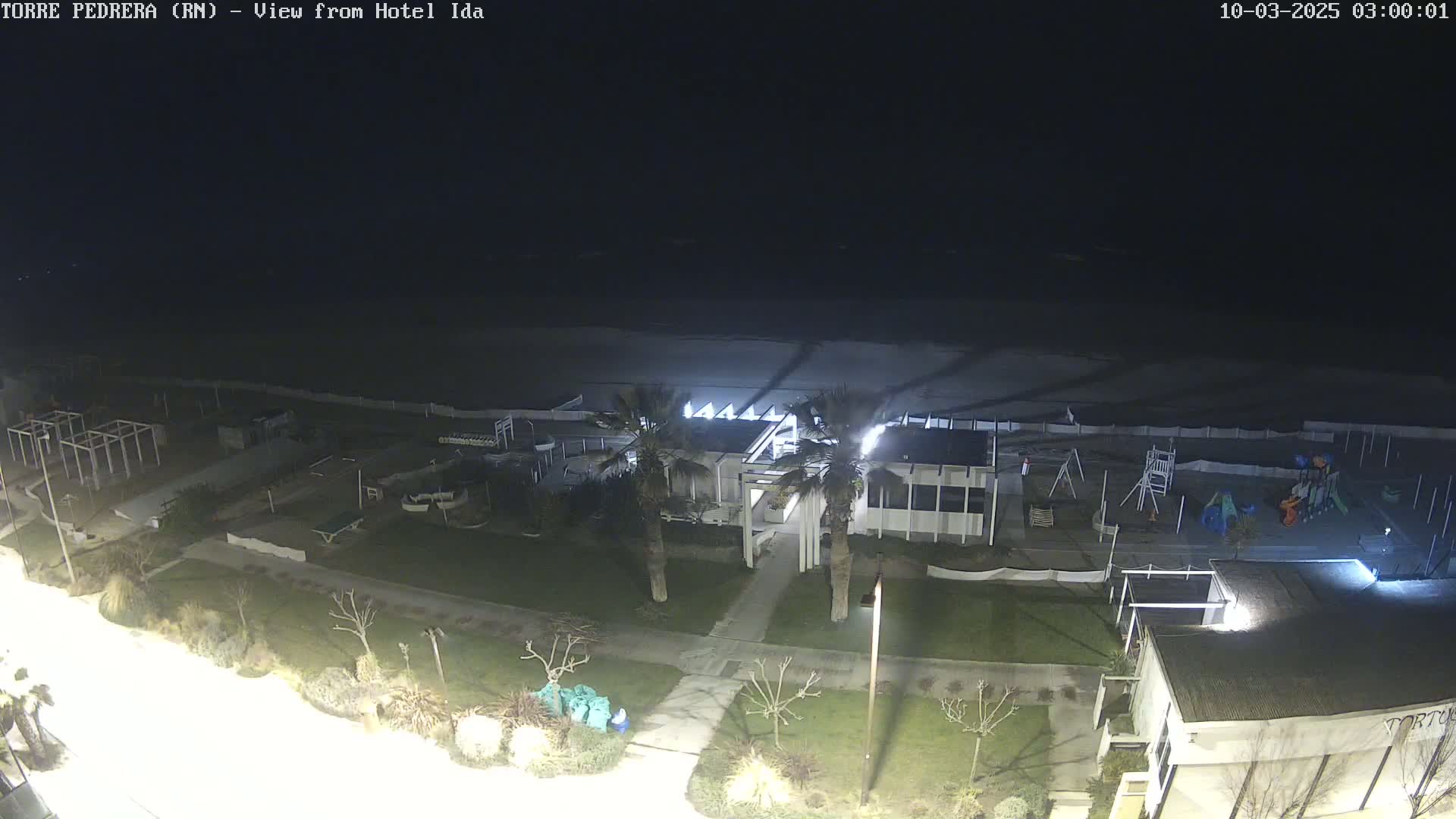 A nighttime view of a beach, a playground, and a building complex with palm trees, all illuminated by artificial light.
