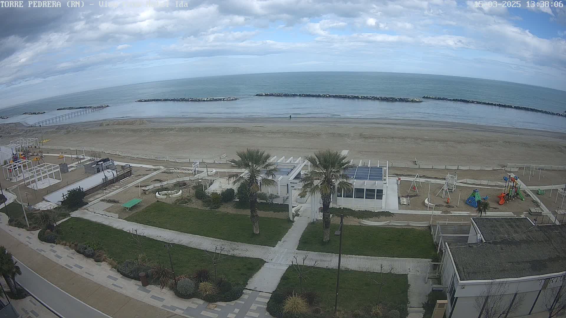 A beach with a playground and a white building is seen under a partly cloudy sky.
