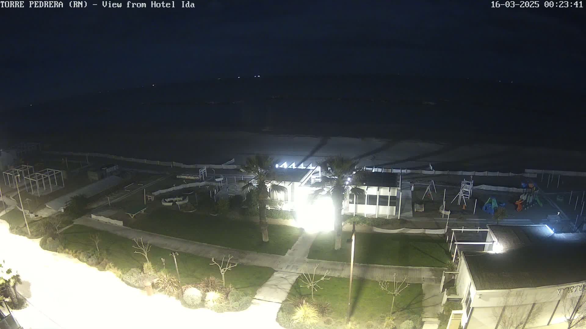 A nighttime aerial view shows a beach, a playground, some buildings, and palm trees under a dark sky.