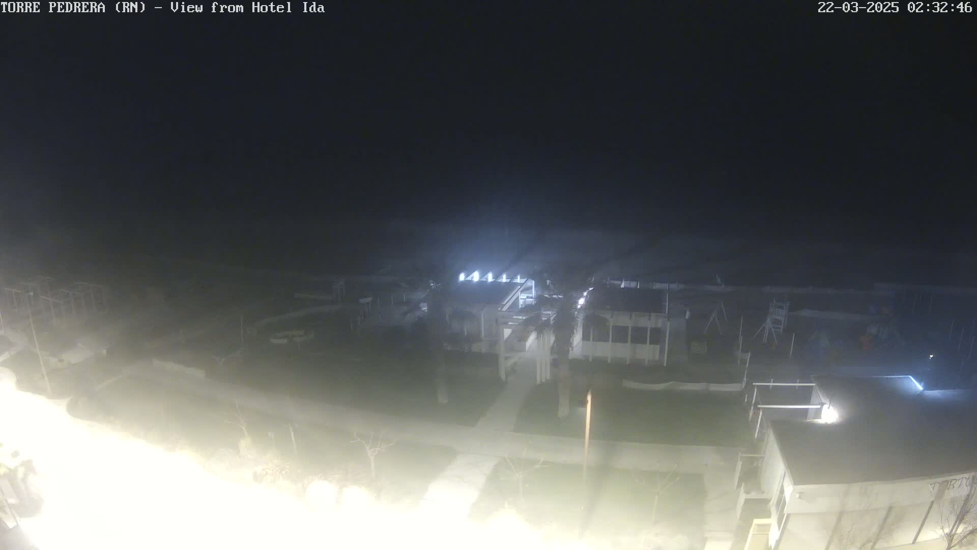A nighttime, hazy view of a building complex with surrounding grounds and sparse vegetation.