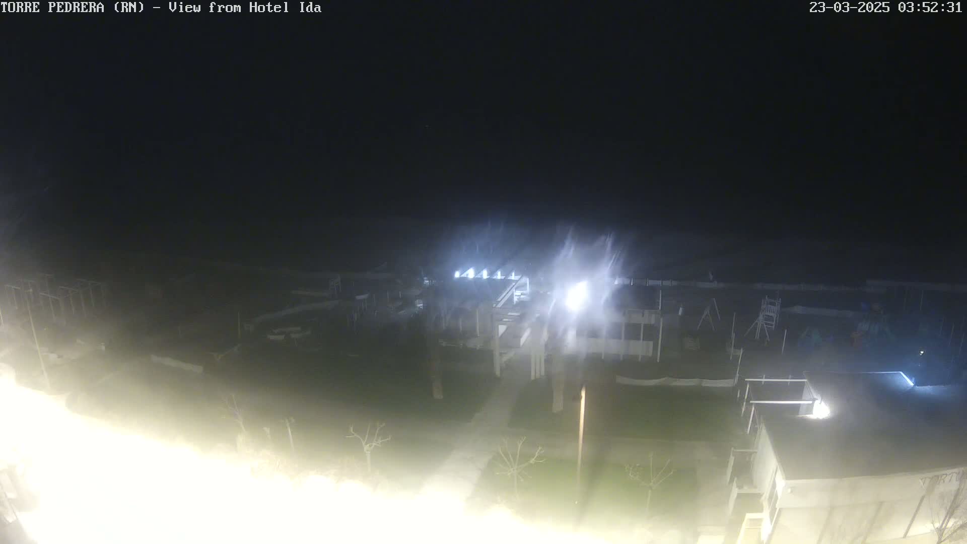 A nighttime, blurry view of a building complex and surrounding grounds, with wind or blowing snow obscuring the scene.