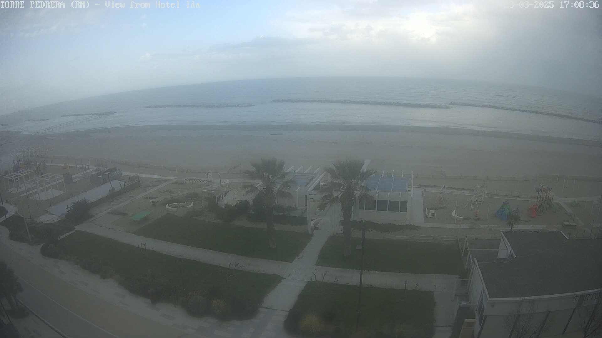 A hazy view shows a beach with a playground and buildings, under an overcast sky.