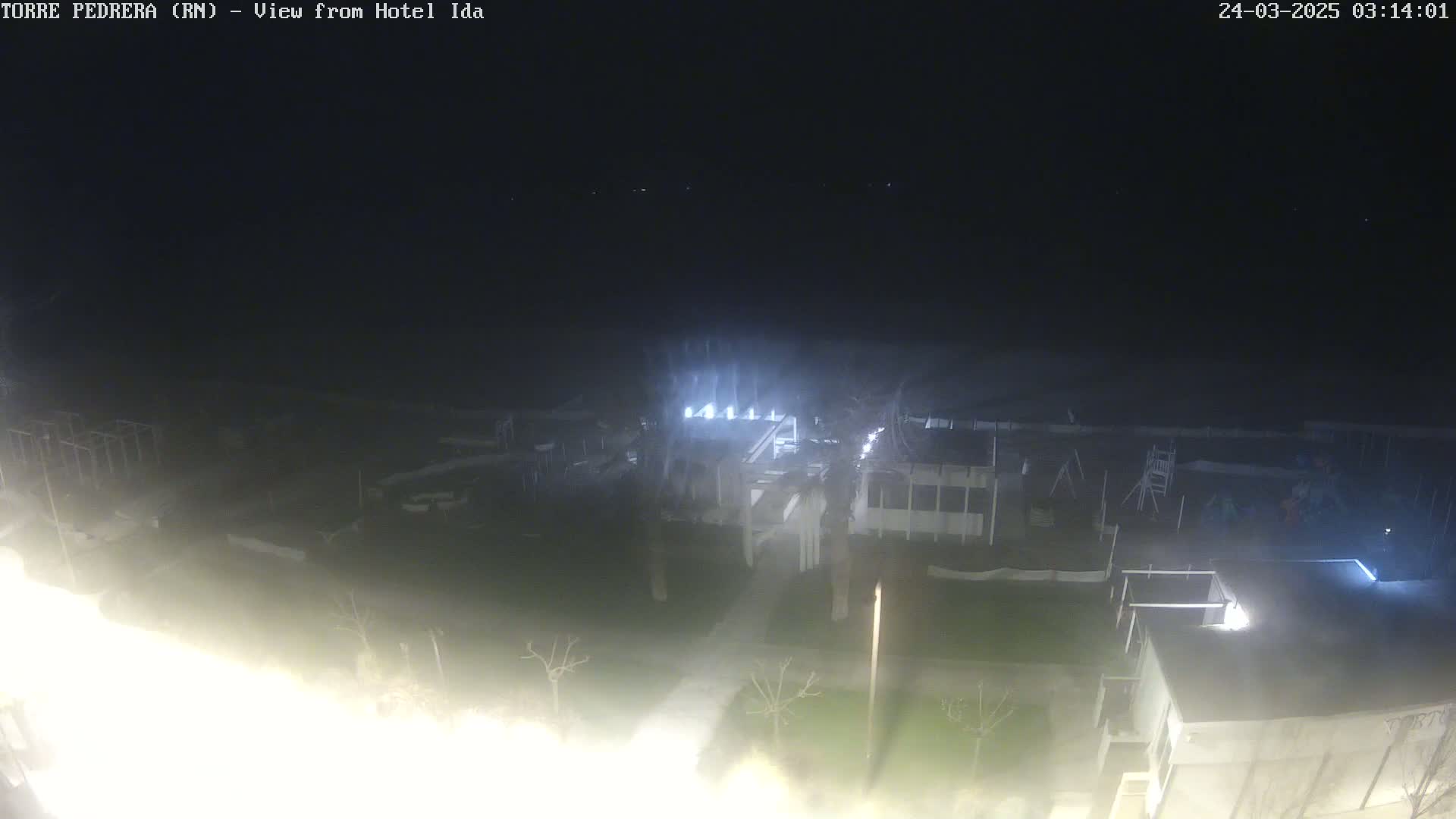 A nighttime aerial view shows a dimly lit complex of buildings and an outdoor play area under a dark, clear sky.