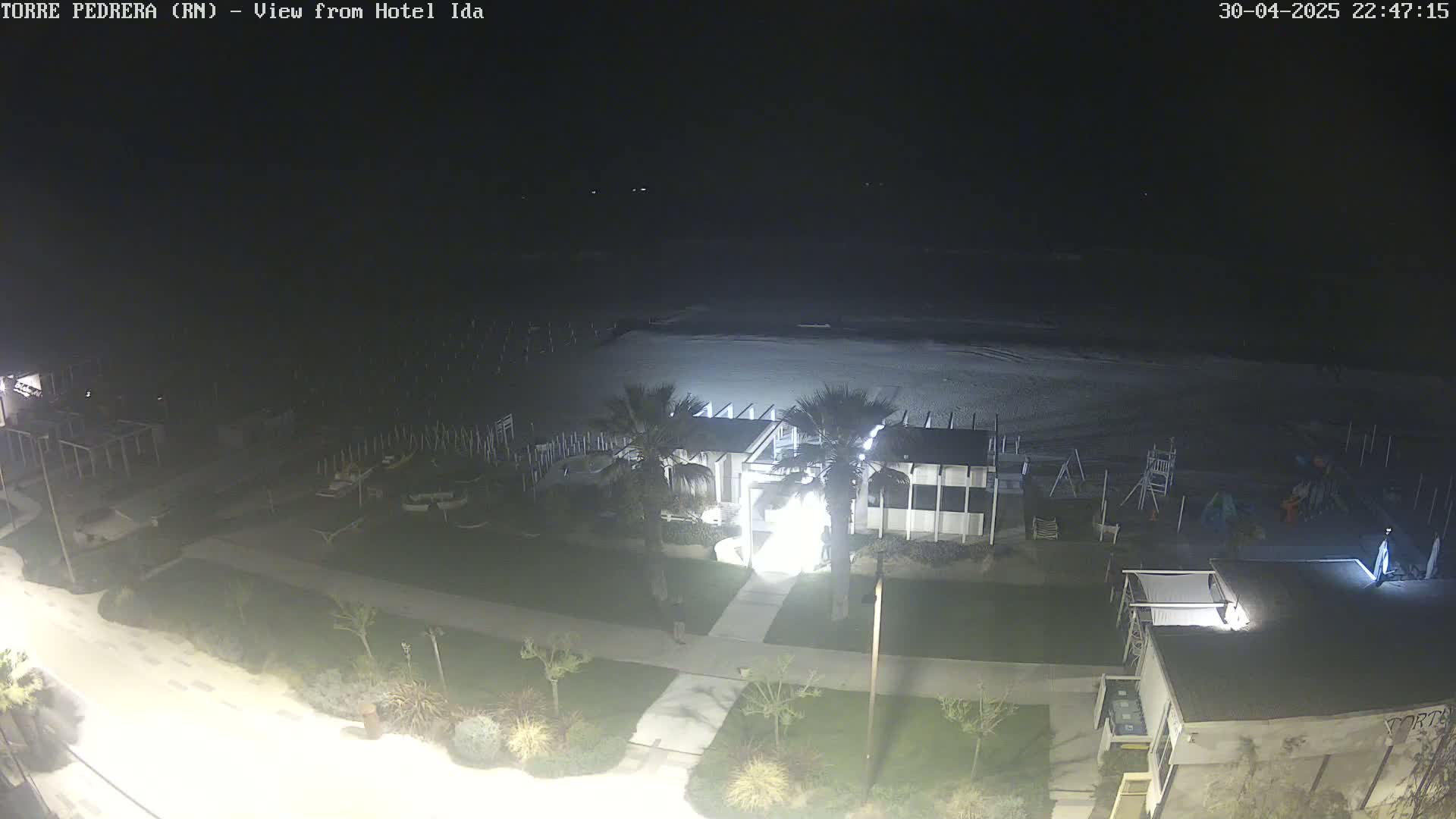 A nighttime view of a beach with a building and some palm trees, illuminated by artificial light.