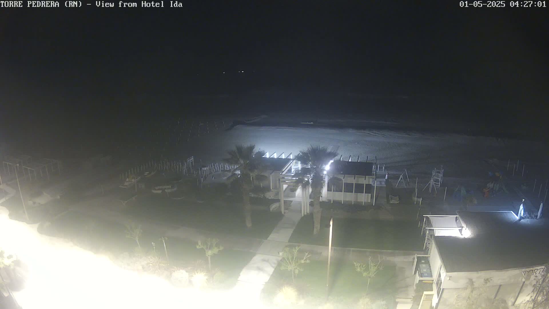 A nighttime view of a beach with a building and some palm trees, under a dark sky.