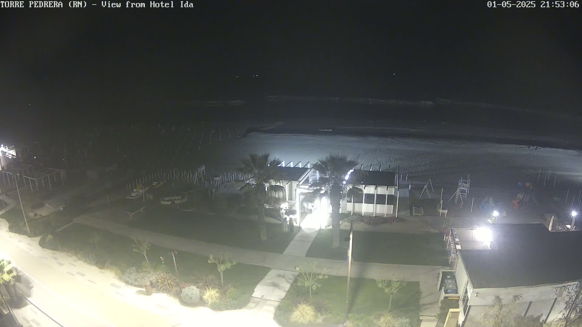 A nighttime view of a beach with a building and palm trees, illuminated by artificial lights.