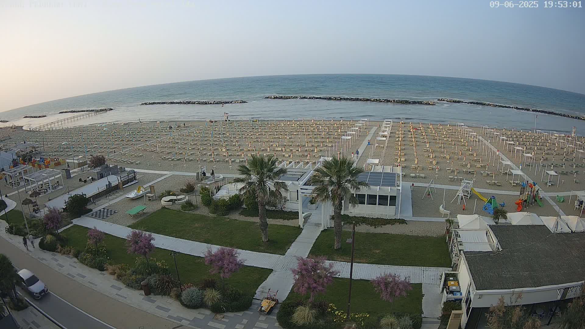 A beach with rows of umbrellas and lounge chairs, a playground, and a beachfront building is visible under a clear, twilight sky.