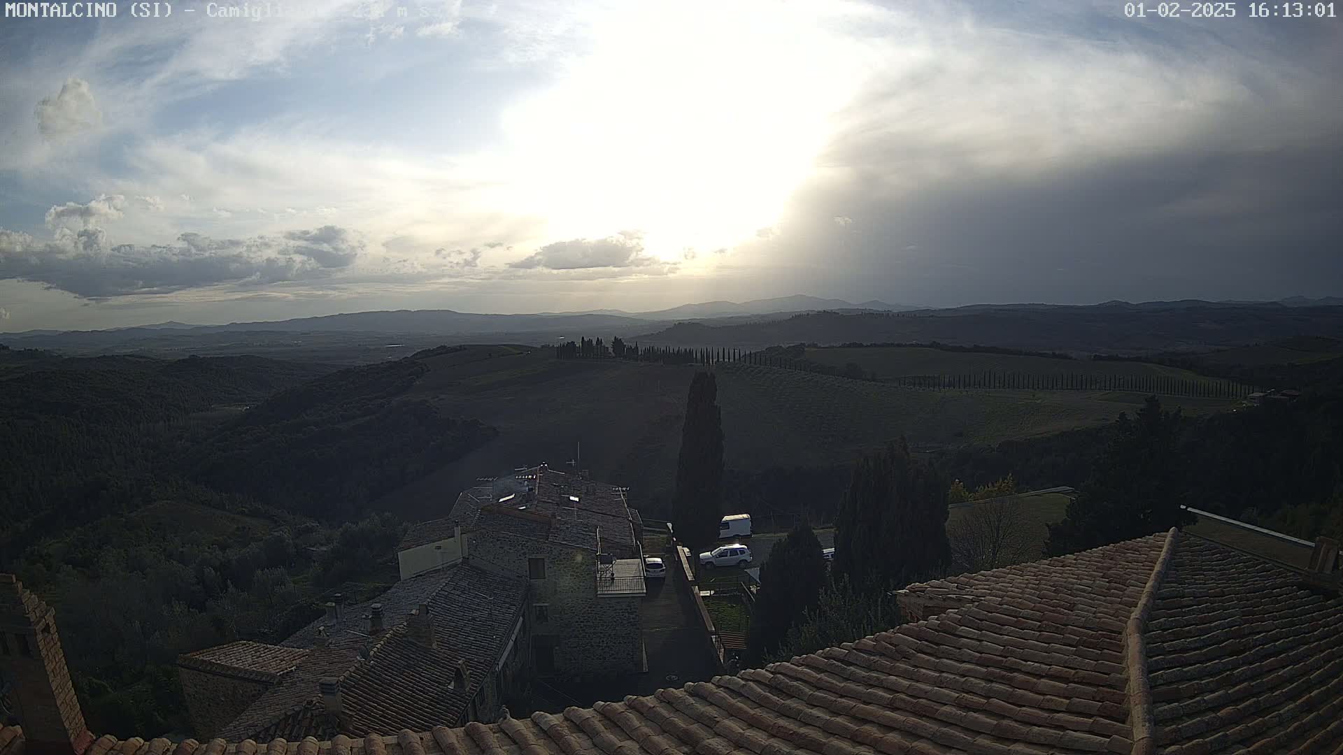 A partly cloudy sunset over rolling hills and a Tuscan village, viewed from a rooftop.