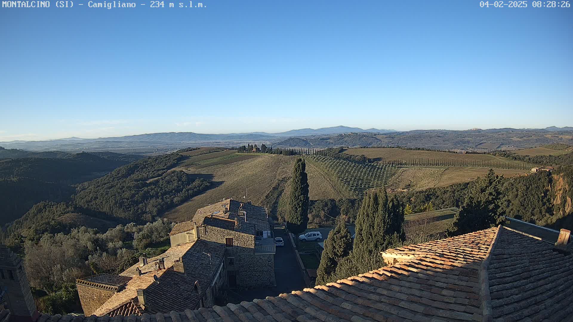 A clear, sunny day reveals a panoramic view of rolling hills, dotted with trees and buildings, from a high vantage point overlooking terracotta rooftops.