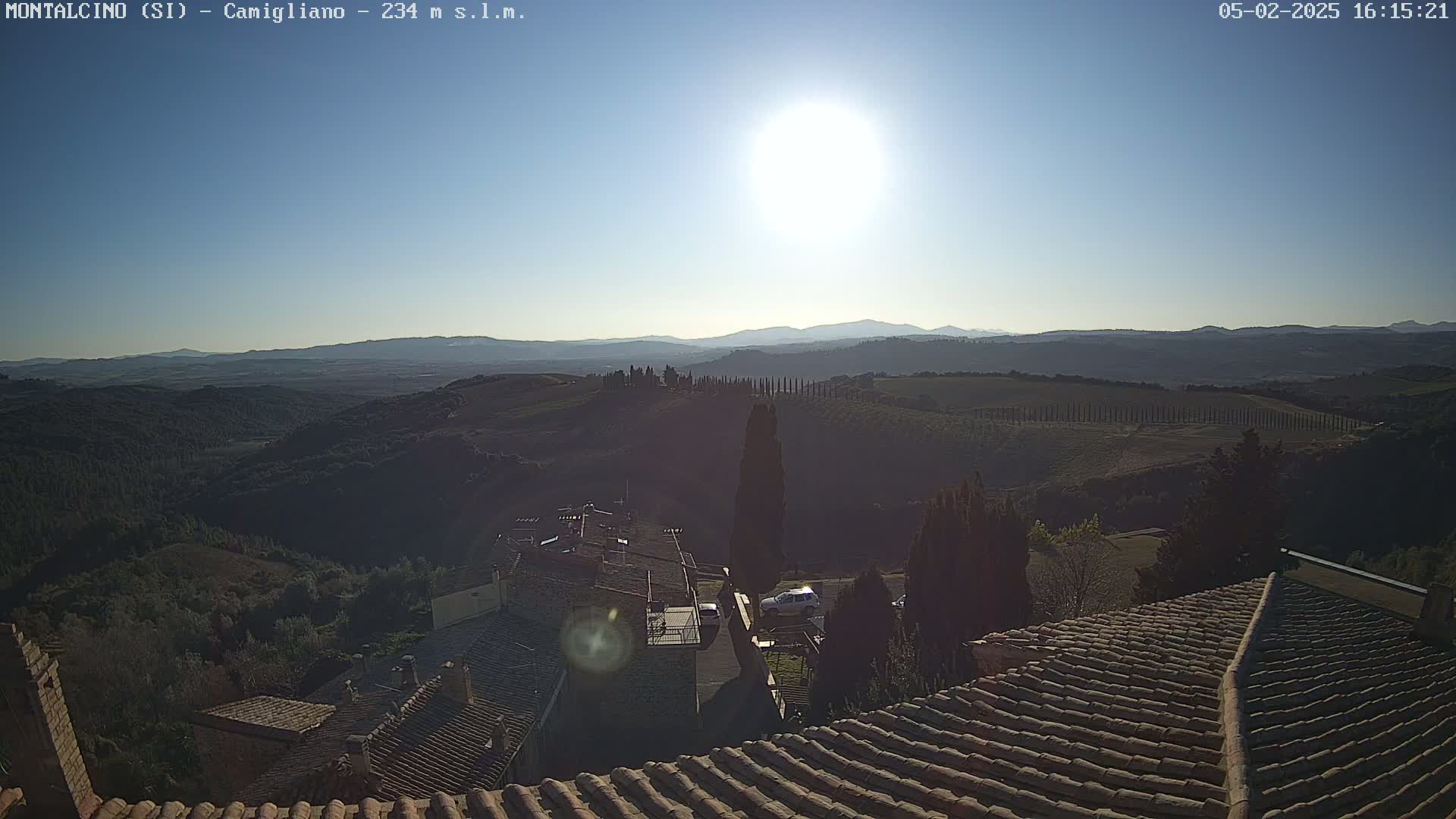 A sunny day reveals a sweeping view of rolling hills and a village with terracotta rooftops, all under a bright, clear sky.