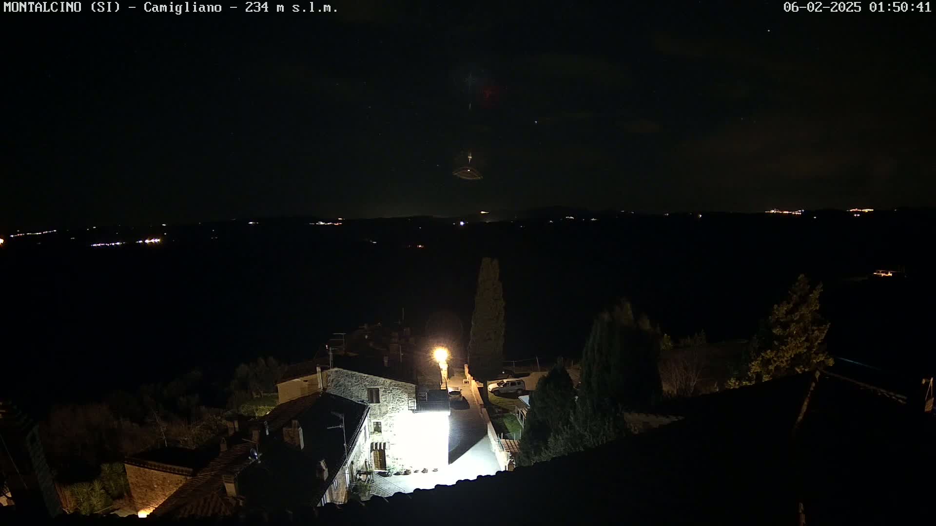 A nighttime, high-angle view of a small village with a few illuminated buildings and a starry sky.
