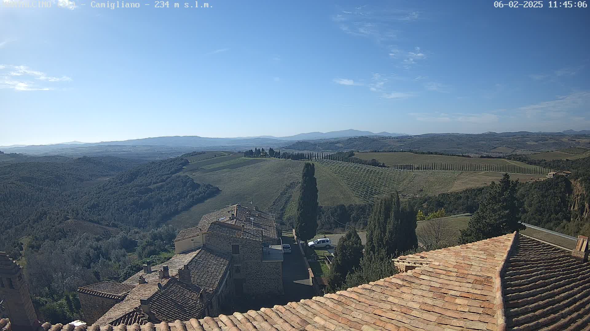 A view from a tiled rooftop shows a hilly landscape with rows of trees under a clear blue sky.