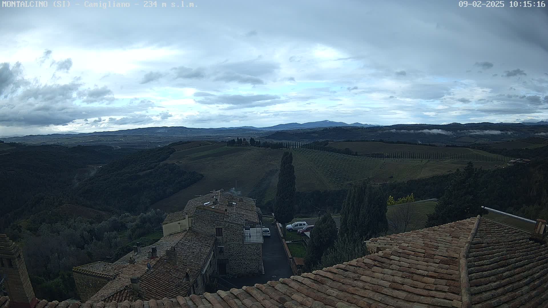 A view from a rooftop shows rolling hills and distant mountains under a mostly cloudy sky.