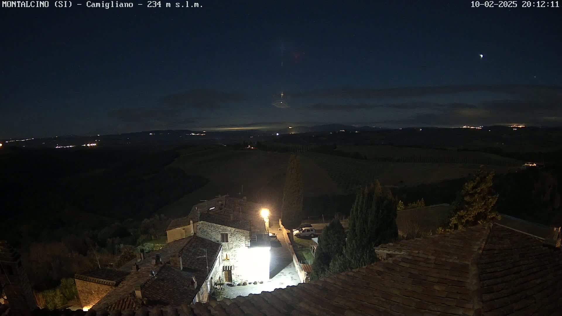 A nighttime view of a small village nestled in rolling hills under a clear, starry sky.