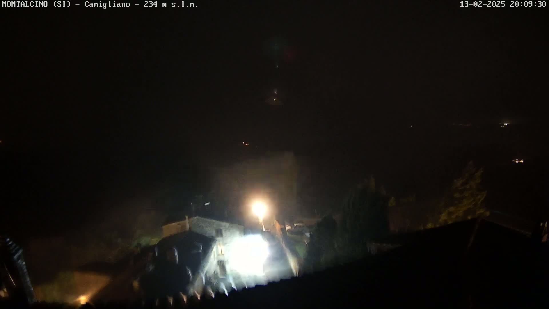 A nighttime, foggy view of a brightly lit building and surrounding area.