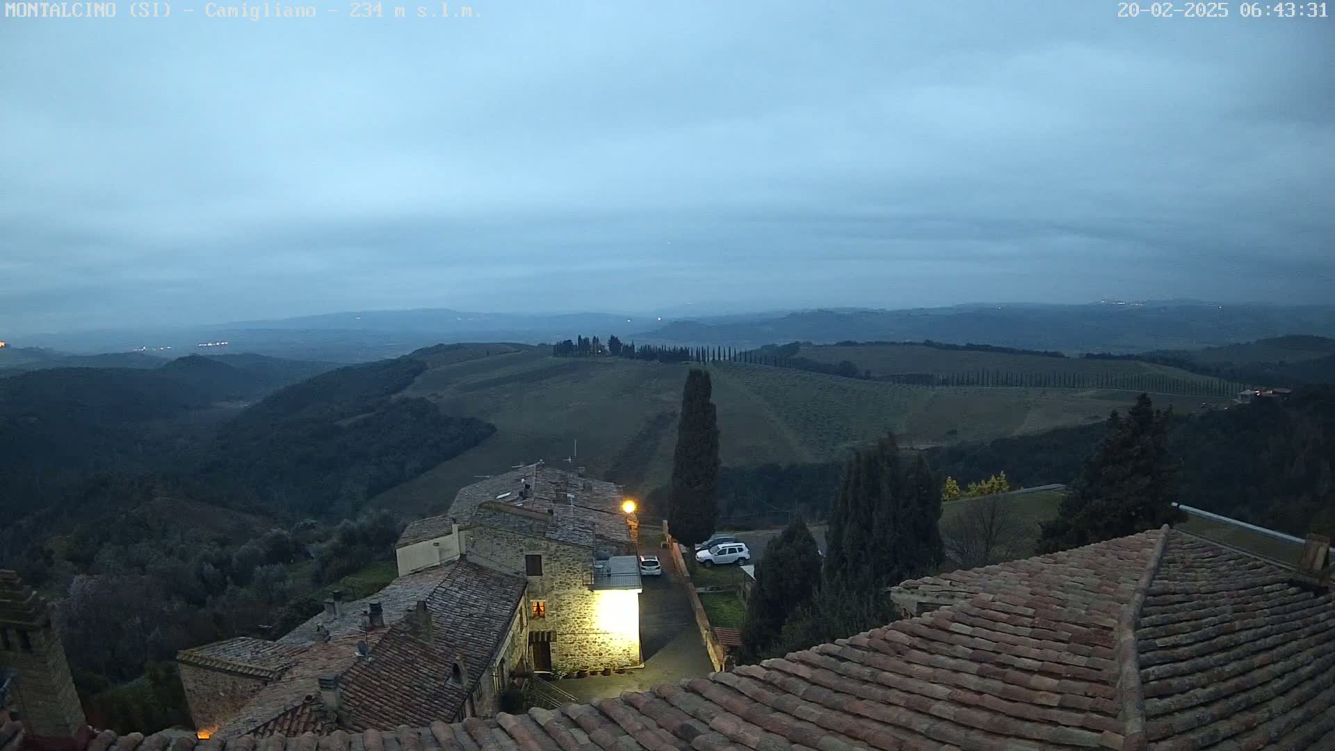 A view from a rooftop shows a village nestled in rolling hills under a twilight sky.