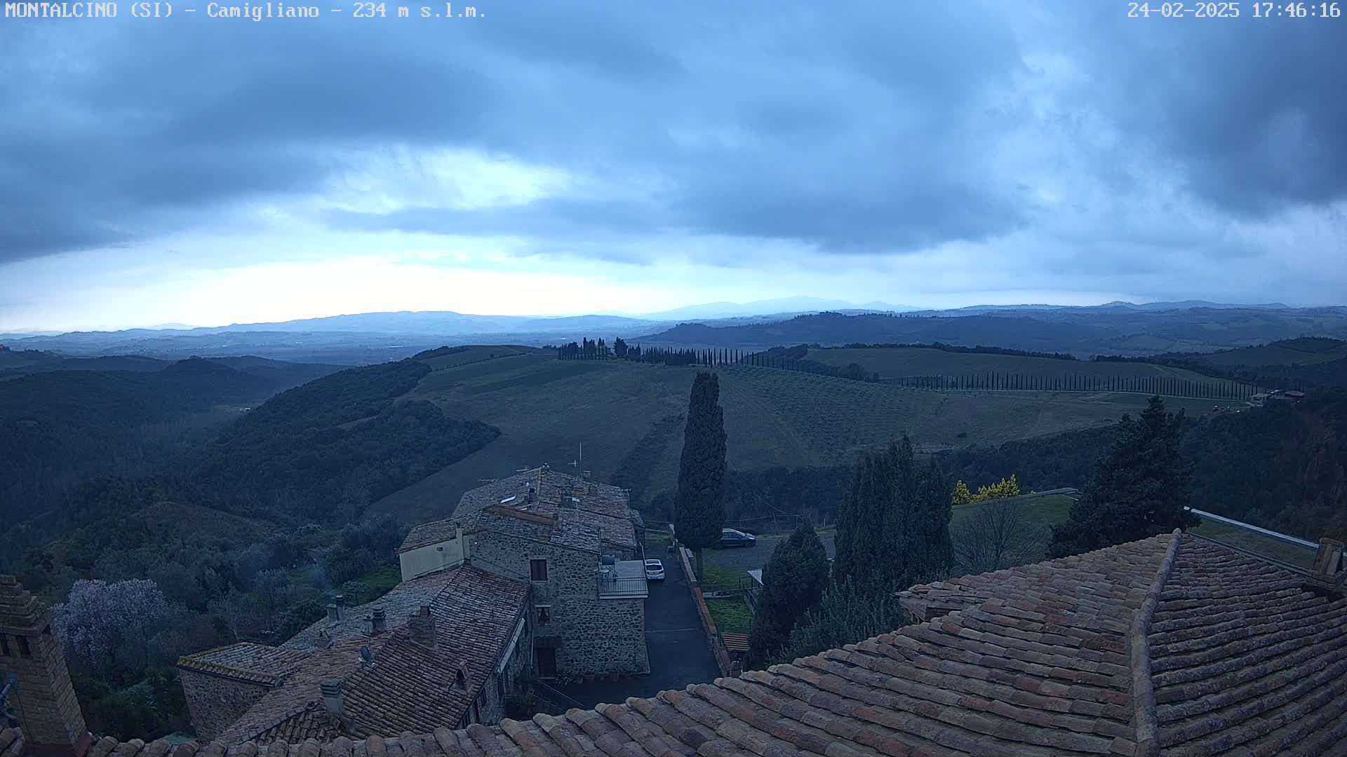 Overcast skies and a hilly landscape are visible from a high vantage point overlooking a village with terracotta roofs.