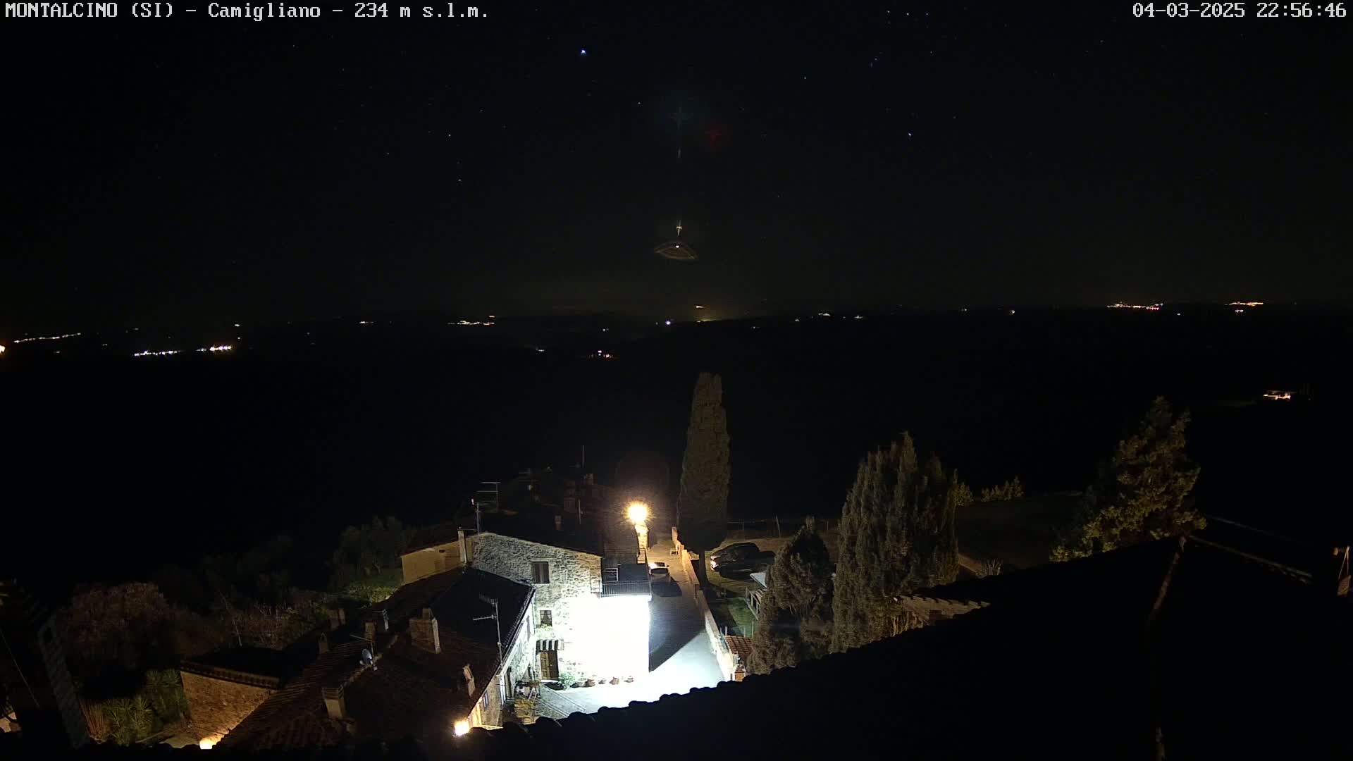 A nighttime view of a small village illuminated by lights, under a clear, starry sky.