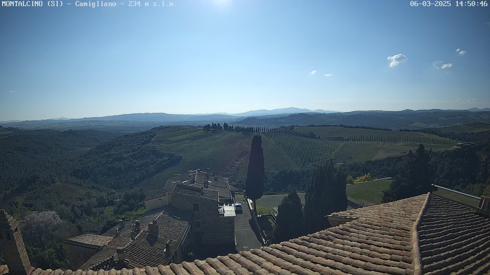 A sunny view from a tiled rooftop shows rolling hills, vineyards, and a village in the distance under a mostly clear sky.
