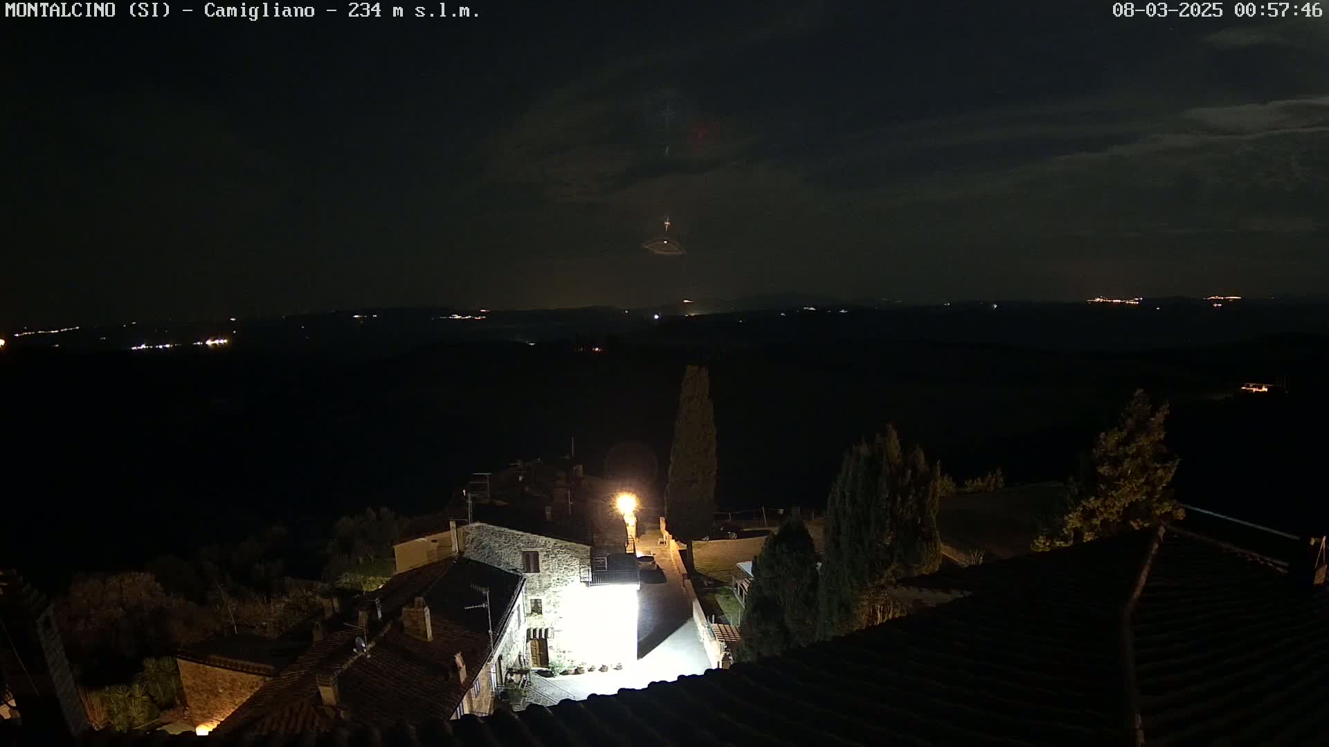 A nighttime view of a small village illuminated by streetlights, overlooking a dark, distant landscape under a mostly clear sky.