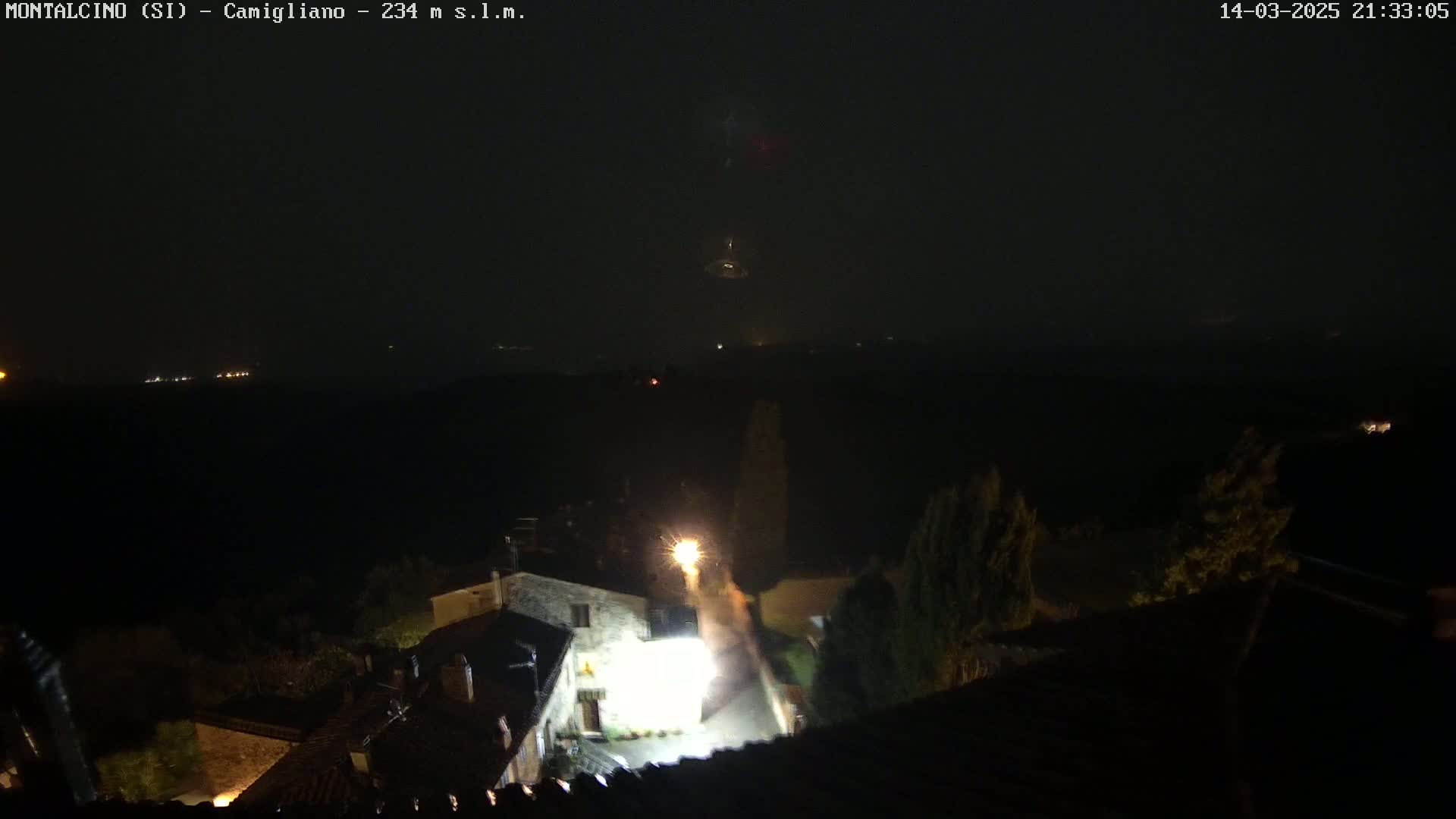 A nighttime, hazy view of a small village nestled in a valley, illuminated by scattered lights.