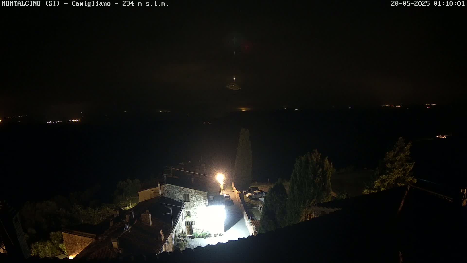 A nighttime view of a village illuminated by a single bright streetlight, with a dark, possibly foggy or cloudy sky above.