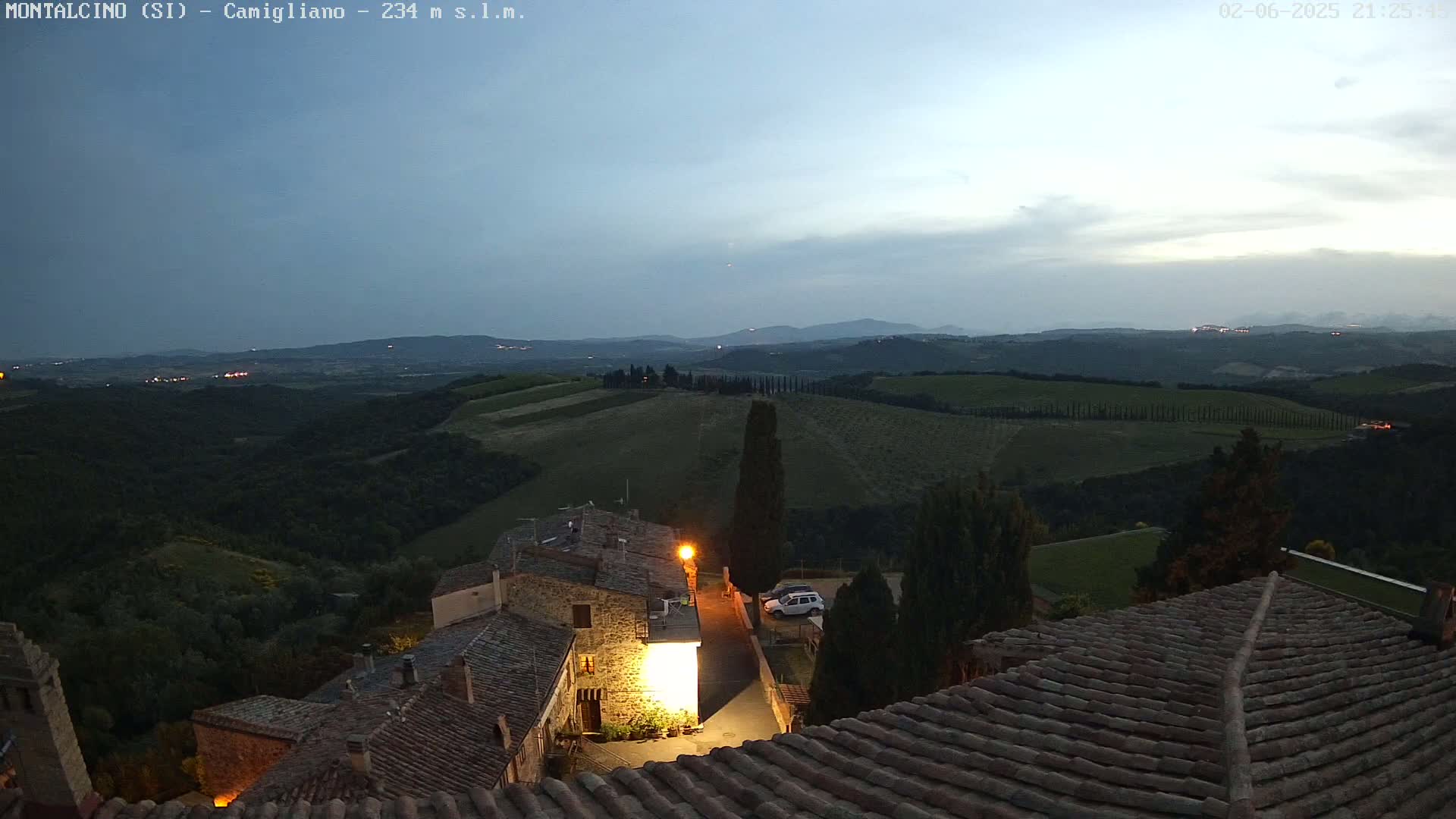 A twilight view from a rooftop shows a small village nestled in rolling hills under a mostly clear sky.