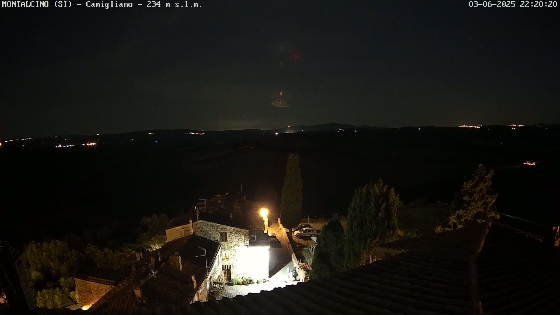 A nighttime view of a village nestled in a dark landscape under a clear, starry sky.